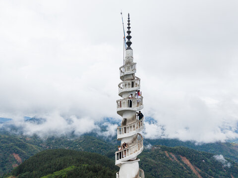 Gampola, Sri Lanka - 22 February 2026: Aerial view of Ambuluwawa Tower with tourists climbing the spiral staircase overlooking misty green hills and lush forests under a cloudy sky.