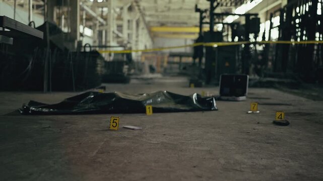 Yellow crime scene markers and body bag at industrial investigation site