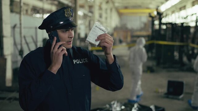 Young police officer holding evidence while talking with superiors by phone
