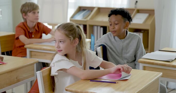 Multicultural children sit at wooden desks with notebooks and pencils, smiling during peer interaction, classroom activity, and early learning confidence together on first day of school routine.