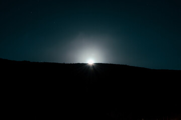 Long exposure car light trails beneath moonlit starry night sky in hilly landscape © CL Productions