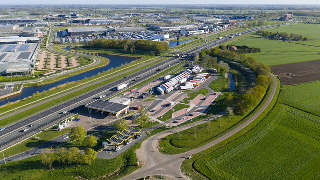 Zwolle, Netherlands - 23 April 2026: Aerial view of Fastned Charging Station and a highway rest area with parked trucks next to the A28 motorway surrounded by green fields.