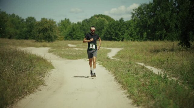 Athlete Runner Participating In Marathon Competition Running Along Dirt Road. Contestant Exercising Cross Country Race.  Sports Event