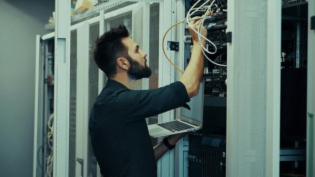 Engineer Holding Laptop Configuring Hardware Equipment In Server Room. IT Specialist Connecting Network Cables In Data Center