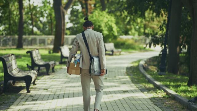 Fired Businessman Walking In Park Carrying Box With Personal Belongings. Dismissed Employee Leaving Job Crisis. Unemployment
