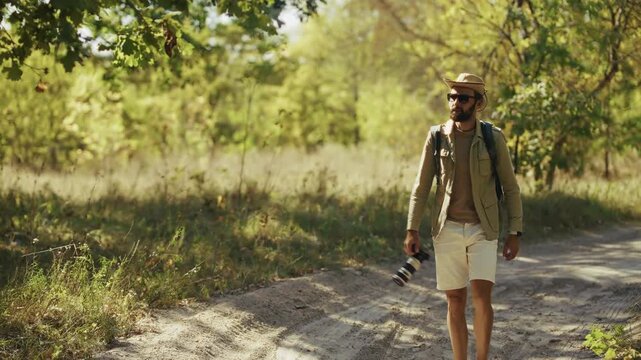 Taking Pictures With Professional Camera On Country Road In Sunny Forest. Traveler With Backpack Shooting Nature Landscapes In Park