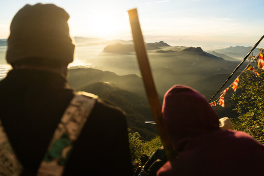 View of Adam's Peak at sunrise with people looking over misty mountain ranges and Buddhist prayer flags in Ratnapura, Sabaragamuwa Province, Sri Lanka.