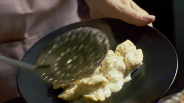 Cook Placing Boiled Dumplings In Cream Sauce Onto Plate. Hot Gnocchi. Italian Culinary