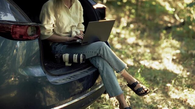 Photographer Sitting In Car Trunk Transferring Photos From Camera To Laptop. Remote Professional Worker Editing Pictures