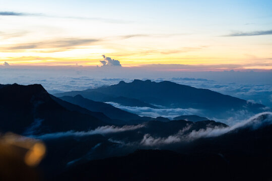 View of Adam's Peak mountain ridges silhouetted against a golden sunrise sky above a thick layer of clouds in Ratnapura, Sabaragamuwa Province, Sri Lanka.