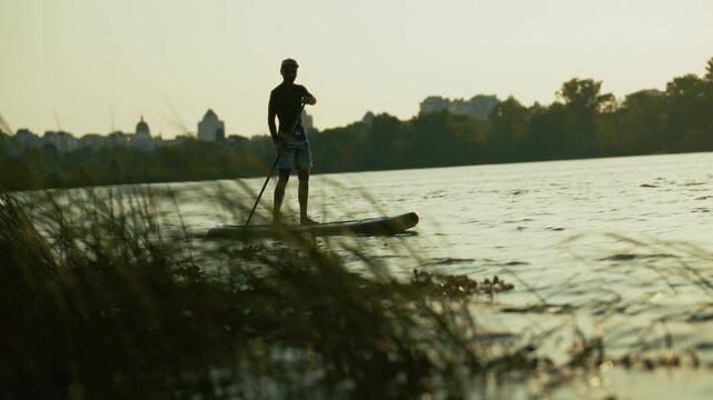 Silhouette Of Surfer Standing On Paddleboard Rowing With Paddle In River Water At Sunset. Summer Water Sport Recreation Activity