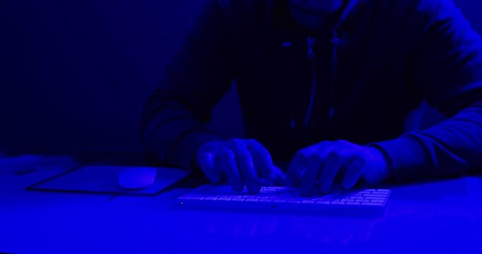 Hooded Hacker Using Mouse and Keyboard in Blue Neon Light