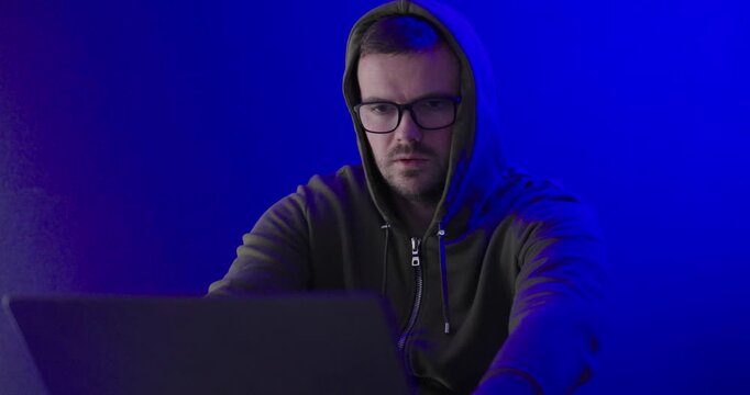 Hooded Man Thinking at Laptop in Blue Neon Cybersecurity Scene