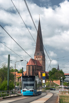 A blue tram passes St Peter's Church on a city street in Rostock, Mecklenburg-Western Pomerania, Germany.