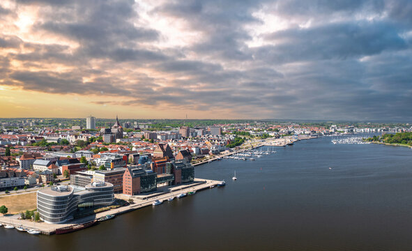 A dramatic aerial view shows Rostock harbor, the Warnow River, marina piers and old town rooftops in Mecklenburg-Western Pomerania, Germany.