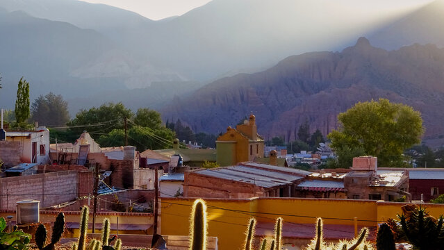 Tilcara, Jujuy, Argentina - April 11, 2023: High angle view of Tilcara village rooftops with mountains and golden sunset light reflecting on cacti in Jujuy, Argentina.