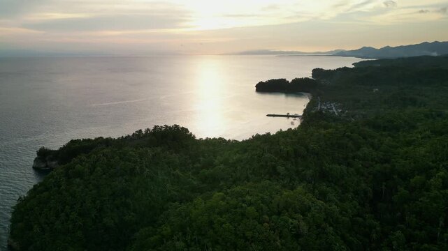 Aerial orbit of Virac, Bicol, Catanduanes with a lush tropical island coastline, calm bay, and shoreline during sunset - Philippines