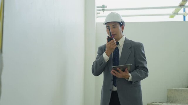 Construction worker hard hat business suit walkie talkie tablet indoor site safety inspection engineer male professional building site communication interior white wall