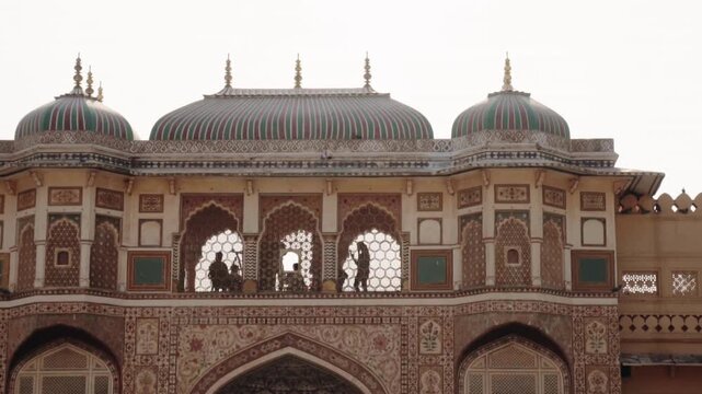 Intricate architecture of the famous Patrika Gate in Jaipur, India, with silhouetted figures of people visible through the ornate arched windows against a bright sky, showcasing a popular landmark