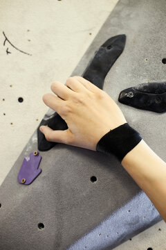 Vertical shot of hand gripping climbing hold on indoor bouldering wall, training strength and focus. Suitable for fitness marketing, sports club promotion, vertical