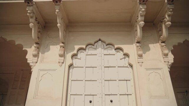 Slow descending view of a historic Indian palace facade showcasing ornate carved sandstone balconies, arched doorways and intricate stonework bathed in bright sunlight, rich in heritage