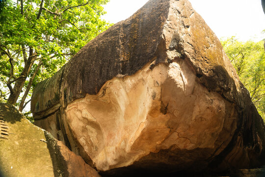 View of the ancient Cobra Hood Cave rock formation with weathered plaster and historical markings surrounded by lush green trees in Sigiriya, Central Province, Sri Lanka.