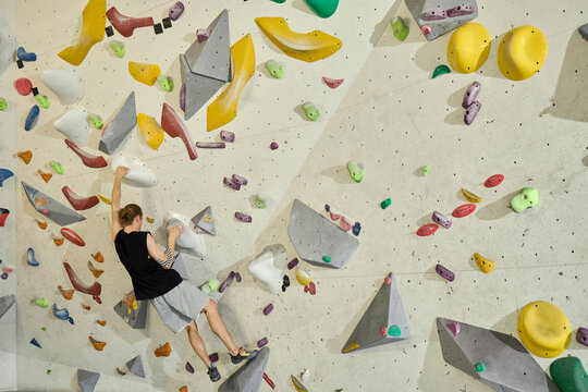 Wide shot of young adult man climbing indoor bouldering wall, training strength, balance, endurance in fitness gym