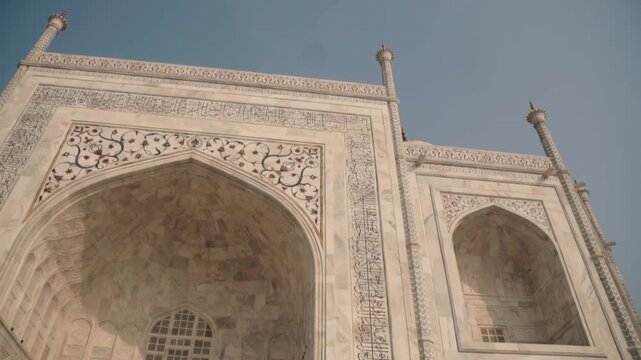 Majestic white marble facade of the Taj Mahal in Agra, showing intricate details of the great gate and arched iwans against a clear blue sky, capturing the essence of Mughal architecture