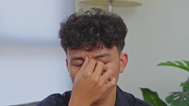 Young Asian man pinching bridge of nose with closed eyes suffering from headache or vertigo