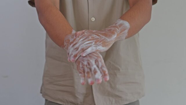 Close-up of hands thoroughly washing soapy hands against neutral background