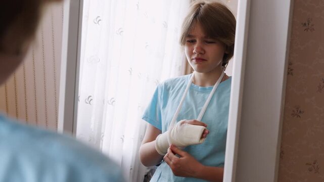 Girl looks at injured hand in mirror while feeling sad at home