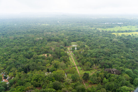 View of the ancient royal gardens and symmetrical pathways surrounded by dense tropical jungle and misty hills in Sigiriya, Central Province, Sri Lanka.