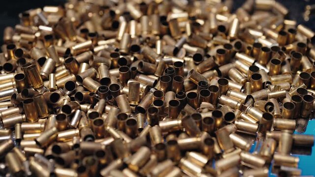 Golden bullet shells sorting and moving on a blue conveyor belt during the ammunition manufacturing process in a factory. Empty brass casings are being shaken in slow motion for quality control