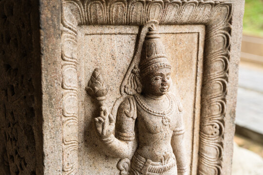 View of an intricate ancient stone carving of a deity holding a lotus flower on a temple pillar Kandy, Central Province, Sri Lanka.