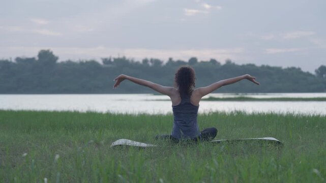 A slow-motion of a South Asian Woman in backbend doing yoga by a calm lake at twilight