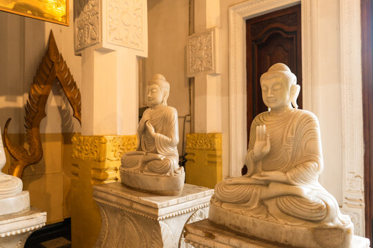 View of serene white marble Buddha statues in meditative poses within a temple interior featuring ornate pillars and warm lighting in Kandy, Central Province, Sri Lanka.