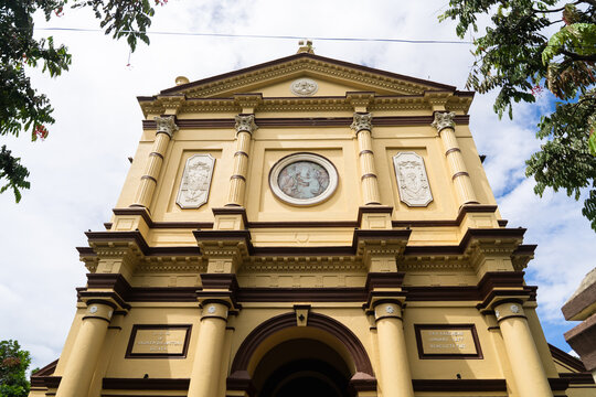 View of the historic St. Anthony's Cathedral featuring a yellow facade with classical columns and religious artwork under a cloudy sky in Kandy, Central Province, Sri Lanka.