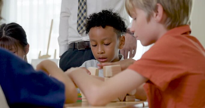 Elementary boys work with colorful blocks at group desk while male teacher monitors nearby, back to school classroom activity builds teamwork, concentration, friendship, problem solving skill