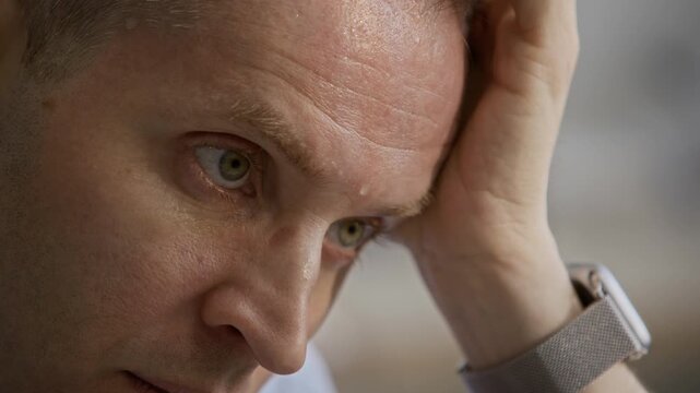 Close up of Caucasian worker perspiring from heat while working in stuffy office. Drop of sweat running down on his forehead