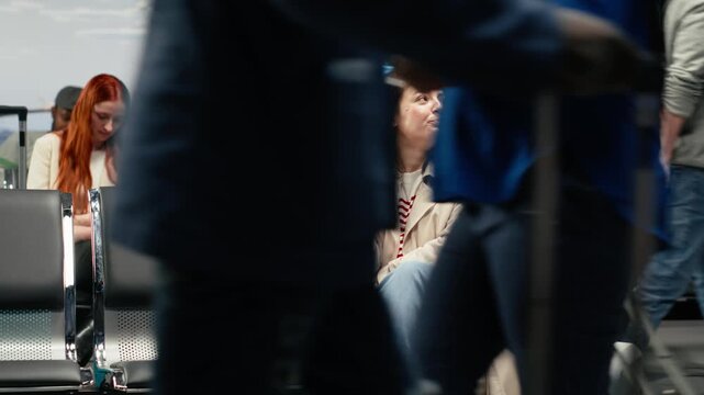 A female traveler rests her feet on a hard shell suitcase and uses her phone while waiting in the airport terminal.