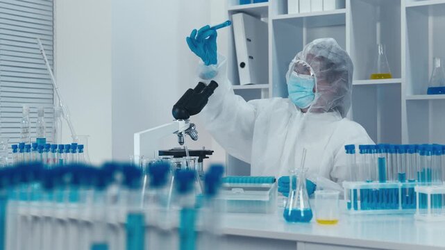 Researcher wearing full protective gear examines test tube in high tech laboratory filled with scientific equipment. Cutting edge medical research, laboratory safety protocols are demonstrated