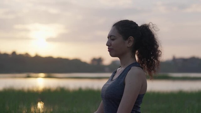 A wide-angle shot of a South Asian woman performing a graceful backbend on her yoga mat beside a quiet lake at sunrise