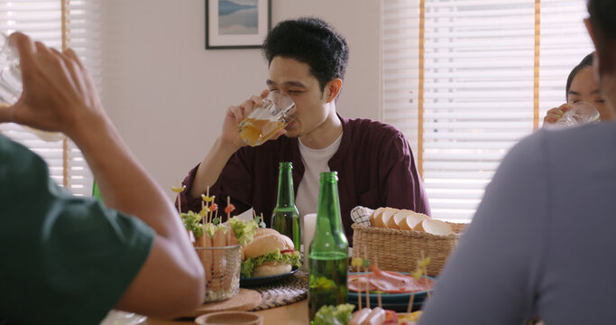 Happy hour good warm summer time diner indoor home. Group of asia people young adult friend man and woman sit at dining table joy fun talk or eat food and drink beer alcohol bottle glass inside house.