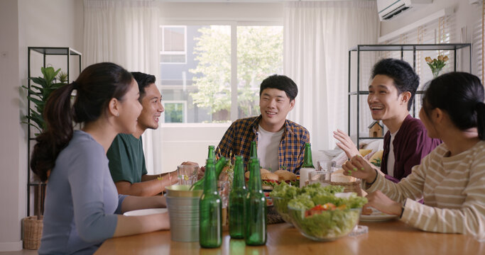 Happy hour good warm summer time diner indoor home. Group of asia people young adult friend man and woman sit at dining table joy fun talk or eat food and drink beer alcohol bottle glass inside house.