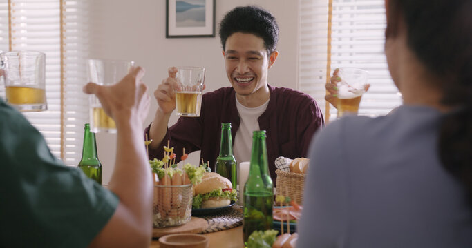Happy hour good warm summer time diner indoor home. Group of asia people young adult friend man and woman sit at dining table joy fun talk or eat food and drink beer alcohol bottle glass inside house.