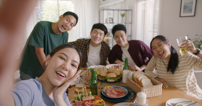 Happy hour diner at home relax smile look at camera shooting video photo on mobile app. Group of asia people young adult friend man and woman sit at dining table joy fun talk or eat food drink beer.
