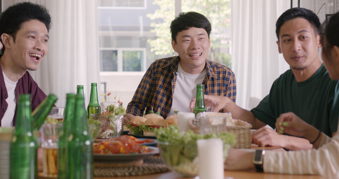 Happy hour good warm summer time diner indoor home. Group of asia people young adult friend man and woman sit at dining table joy fun talk or eat food and drink beer alcohol bottle glass inside house.