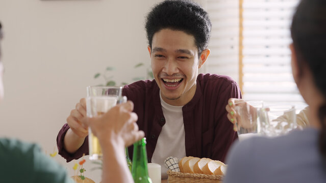 Happy hour good warm summer time diner indoor home. Group of asia people young adult friend man and woman sit at dining table joy fun talk or eat food and drink beer alcohol bottle glass inside house.