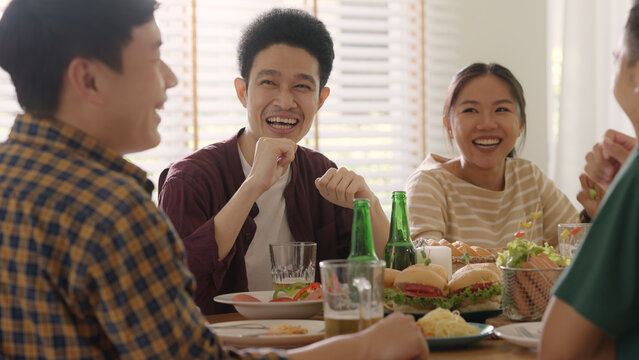 Happy hour good warm summer time diner indoor home. Group of asia people young adult friend man and woman sit at dining table joy fun talk or eat food and drink beer alcohol bottle glass inside house.