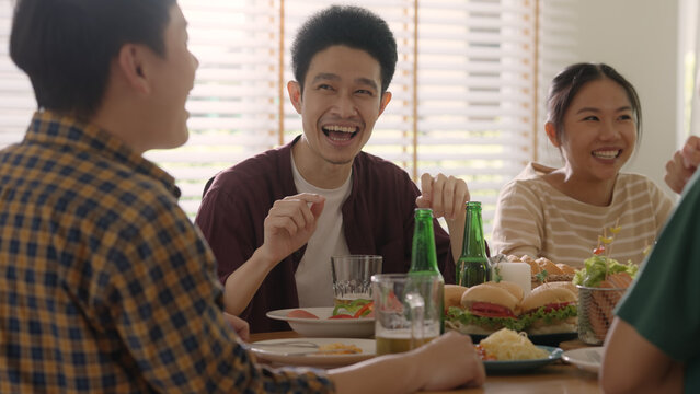 Happy hour good warm summer time diner indoor home. Group of asia people young adult friend man and woman sit at dining table joy fun talk or eat food and drink beer alcohol bottle glass inside house.